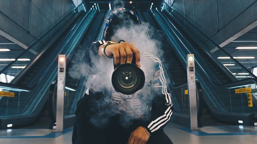 man holding camera while squating with smoke on face inside building